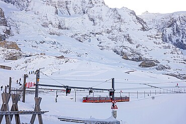 Railroad Cog Train Jungfraubahn in a Snowy Sunny Winter Day and Mountain Peak and Jungfraujoch Observatory Building in Kleine Scheidegg, Grindelwald, Bernese Oberland, Bern Canton, Switzerland