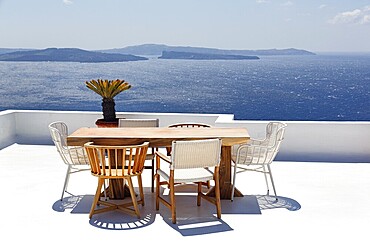 Wooden table and various chairs on a white terrace by the sea, view of the caldera, Oia, Santorini, Cyclades, Aegean Sea, Greece