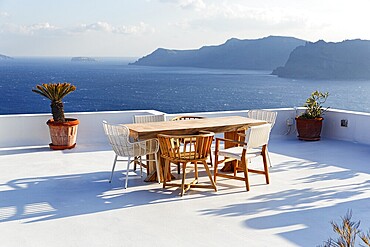 Wooden table and various chairs on a white terrace by the sea, view of the caldera, Oia, Santorini, Cyclades, Aegean Sea, Greece