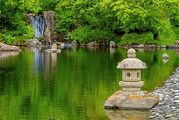 A waterfall and a stone lantern next to a tranquil pond in the Nikka Yuko Japanese Garden in Lethbridge, Alberta, Canada