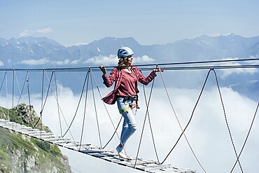 Wanderlust and adventures. Extreme vacation. A woman walks on a suspension bridge high in the mountains at the level of a cloud