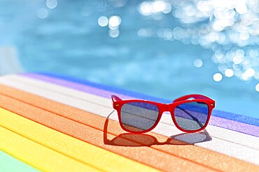 Summer background. Concept for summer and vacation. Red sunglasses by the pool in the background with blue water