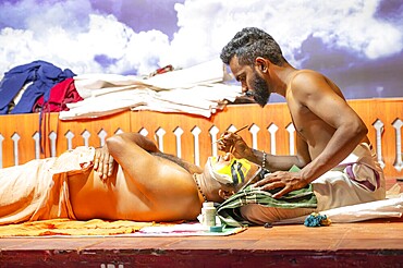 Artist paining face of Kathakali performer with green pachcha color, Kerala, malayalam traditional indian dance, mime, drama and music act, Thekkady in India, 25.03.2025