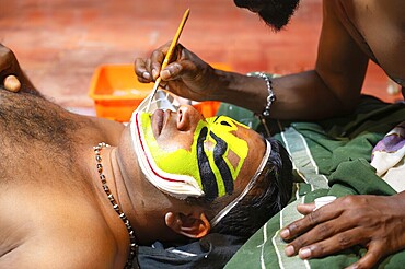 Artist paining face of Kathakali performer with green pachcha color, Kerala, malayalam traditional indian dance, mime, drama and music act, Thekkady in India, 25.03.2025