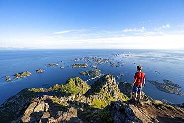 View of numerous small rocky islands with houses, mountaineers on the summit of Festvågtind, view of Henningsvær, Vågan, Lofoten, Nordland, Norway