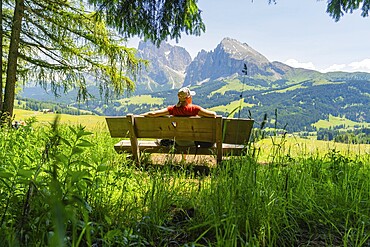 Person relaxing on a bench with a wide view of the mountains and green landscape, Alpe di Siusi, Dolomites, South Tyrol, Italy