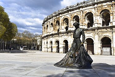 Statue in front of a historic Roman amphitheater under a cloudy sky. Herault, France