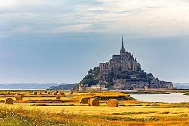 A historic castle under a cloudy evening sky surrounded by fields, Mont Saint Michel in Normandy, France