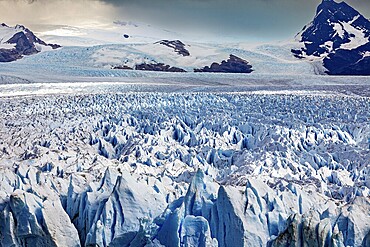 A vast icy landscape stretches out in front of a cloudy sky and majestic mountain peaks, The Perito Moreno glacier in Argentina