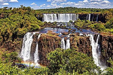 Waterfalls pour down amidst a tropical landscape under a blue sky, The Iguazu Falls between Argentina and Brazil