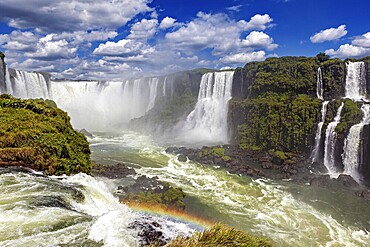 Waterfalls with rainbow over a river under dramatic clouds in the sky, The Iguazu Falls between Argentina and Brazil