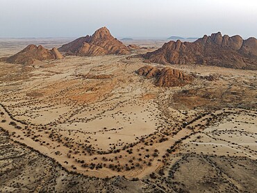 Spitzkoppe (1728 m) - on the left - and Pondok Mountain majestically rise above the surrounding desert plains. At dawn. Aerial view. Drone shot. Damaraland, Namibia