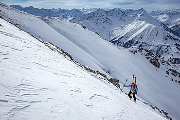 A ski tourer ascending a very steep summit slope, ski tour to the Thaneller, in the background the snow-covered high mountain landscape of the Lechtal Alps, Tyrol, Austria