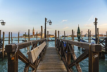 Wooden pier with gondolas and lamps leading to san giorgio maggiore in venice at sunset, creating a romantic and picturesque view