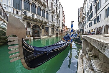 Traditional gondola moored in venice canal with turquoise water, near a bridge and old buildings, showing venetian architecture and lifestyle