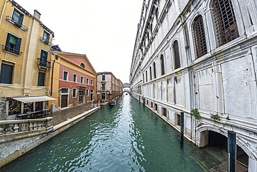 Serene canal in venice with traditional gondola navigating towards distant bridge, showcasing colorful buildings and historic architecture