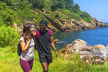 Young couple walking and laughing along a beautiful coastline path on a sunny summer day, enjoying the scenic views