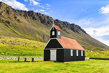 Black wooden church in a meadow in front of a cliff, Saurbæjarkirkja, Saurbær, Rauðisandur, Raudisandur, near Patreksfjördur, Westfjords, Iceland