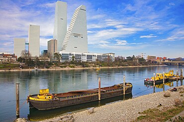 A cargo ship lies on the riverbank in Basel with modern skyscrapers in the background, pharmaceutical company Roche, skyscrapers, towers, Rhine, Basel, Switzerland