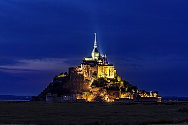 Historic monastery illuminated at night against a dark blue sky, Mont Saint Michel in Normandy, France