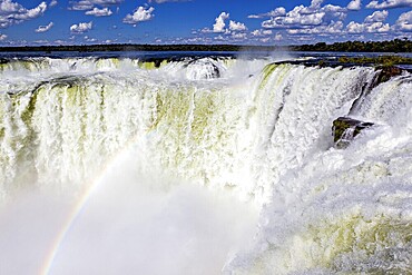 Waterfall with a rainbow over the foaming spray against a cloudy sky, The Iguazu Falls between Argentina and Brazil