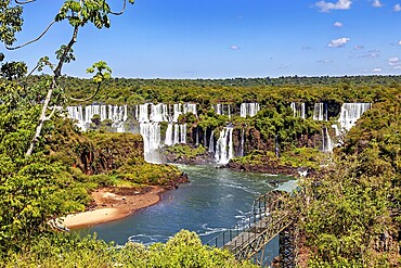 Panorama of the waterfalls with walkway along the river and dense deciduous forest, The Iguazu Falls between Argentina and Brazil