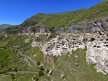 Cave architecture along an elongated rock formation, embedded in a green natural backdrop with road, aerial view, cave town, cave monastery, Vardzia, Vardzia, Samtskhe-Javakheti region, Samtske Javakheti, Lesser Caucasus, Georgia