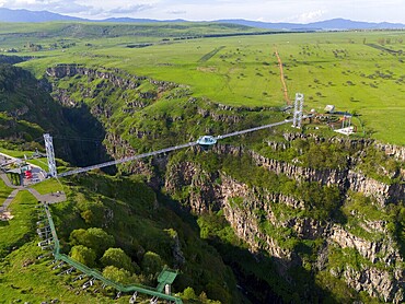 A long bridge with a glass platform spans a deep gorge, surrounded by green landscape and distant mountains, aerial view, Diamond Bridge, Diamond Glass Bridge, world's longest free-hanging construction, Dashbashi Gorge, Khrami River, Tsalka Nature Reserve, Kartlia, Georgia