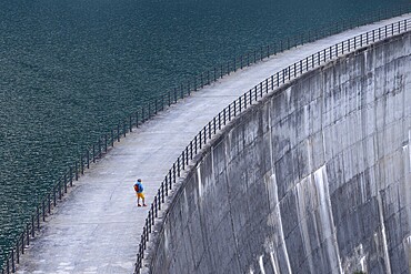 Woman, walking alone along a large dam with a view of the endless expanse of water, Zervreilastausee, Vals, Canton Graubünden, Switzerland