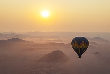 The hot-air balloon above an arid plain and isolated mountain ridges at the edge of the Namib Desert. At sunrise. Aerial view from a second balloon. Kulala Wilderness Reserve, Namibia
