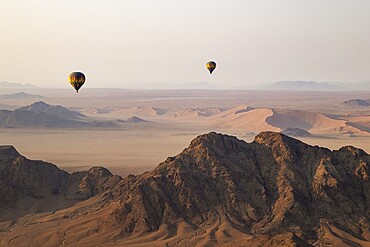 Two hot-air balloons above an arid plain and isolated mountain ridges at the edge of the Namib Desert. Aerial view from another balloon. Namibia