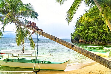 Young man relaxing on a palm tree over a tropical beach in kangbangyo island, siargao, philippines