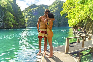 Romantic couple hugging on a pier, enjoying breathtaking view of kayangan lake's turquoise water and lush limestone cliffs