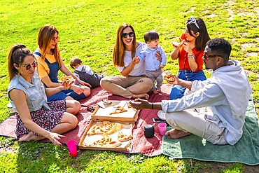Group of cheerful multi ethnic friends and family members enjoying pizza at a picnic in park during a sunny day