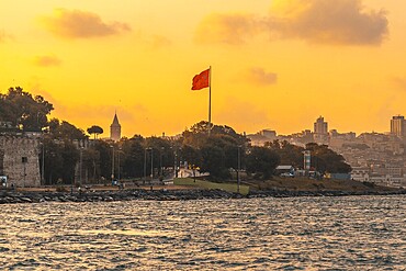 Scenic sunset view of istanbul's cityscape, featuring the prominent galata tower and a waving turkish flag, creating a patriotic and picturesque scene