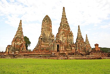 Scenic view of the historical wat chaiwatthanaram temple with its towering prangs and serene green lawn under a cloudy sky in ayutthaya, thailand