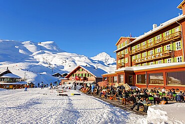 The Famous and Historical Hotel Bellevue des Alpes with People on the Terrace at 2061 Meters High Up and Mountain Peak with Ski Slope in a Sunny Winter Day in Kleine Scheidegg, Grindelwald, Bern Canton, Switzerland