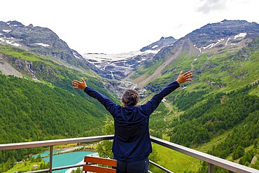 Woman with Arms Outstretched over the Beautiful Mountain Alp Grüm with Glacier and Alpine Lake Palü in the Swiss Alps in a Cloudy Summer Day in Poschiavo, Bernina, Grisons, Switzerland