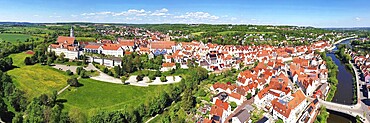 Fascinating aerial view of Donauwörth with its characteristic red roofs and historic buildings. A striking building with a tower stands out in the foreground, surrounded by well-tended green spaces and trees. The town stretches along the rolling hills and offers a picturesque atmosphere with idyllic streets, a historic townscape and expansive landscapes. Donauwörth, Swabia, Bavaria, Germany