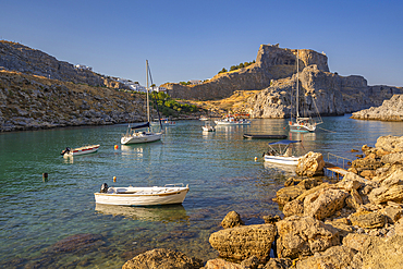 View of sailboats in St Paul's Bay, Lindos and Lindos Acropolis from beach, Lindos, Rhodes, Dodecanese Island Group, Greek Islands, Greece, Europe