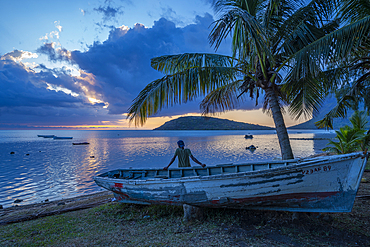 View of local man sat on boat viewing Le Morne from Le Morne Brabant at sunset, Savanne District, Mauritius, Indian Ocean, Africa