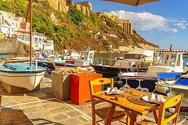 View of restaurant and boats in Marina di Corricella and fortress in background, Procida, Phlegraean Islands, Gulf of Naples, Campania, Southern Italy, Italy, Europe