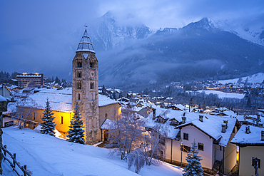 View of Church of Saint Pantalon and the snow covered town centre and mountainous background in winter, Courmayeur, Aosta Valley, Italy, Europe