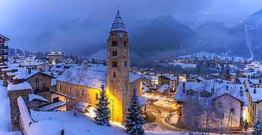 View of Church of Saint Pantalon and the snow covered town centre and mountainous background in winter at dusk, Courmayeur, Aosta Valley, Italy, Europe