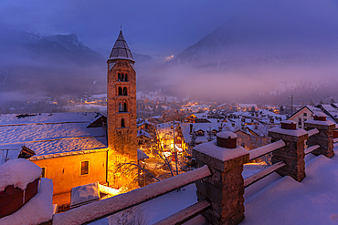 View of Church of Saint Pantalon and the snow covered town centre and mountainous background in winter at dusk, Courmayeur, Aosta Valley, Italy, Europe