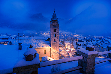 View of Church of Saint Pantalon and the snow covered town centre and mountainous background in winter at dusk, Courmayeur, Aosta Valley, Italy, Europe