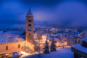 View of Church of Saint Pantalon and the snow covered town centre and mountainous background in winter at dusk, Courmayeur, Aosta Valley, Italy, Europe