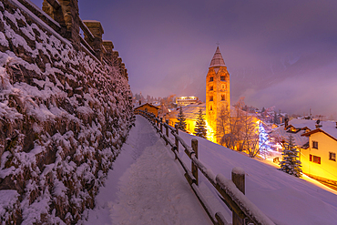 View of Church of Saint Pantalon and the snow covered town centre and mountainous background in winter at dusk, Courmayeur, Aosta Valley, Italy, Europe