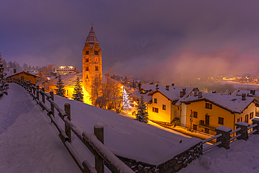 View of Church of Saint Pantalon and the snow covered town centre and mountainous background in winter at dusk, Courmayeur, Aosta Valley, Italy, Europe