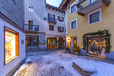 View of shops, town centre and snow covered mountains in Courmayeur at dusk during Christmas, Courmayeur, Aosta Valley, Italy, Europe